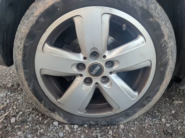 A Mini alloy wheel with a flat tyre on a gravel verge near Burton Joyce