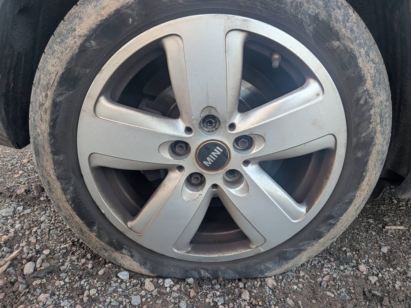 A Mini alloy wheel with a flat tyre on a gravel verge near Burton Joyce