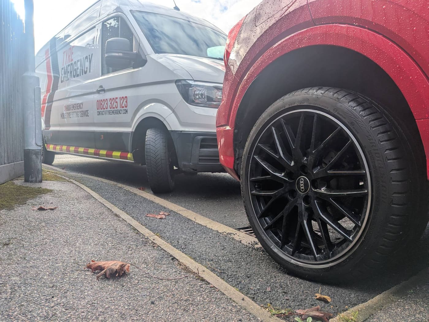 The Tyre Emergency van parked behind a red Audi Q2 at the kerb, the Audi’s black alloy wheel and Bridgestone tyre in the foreground