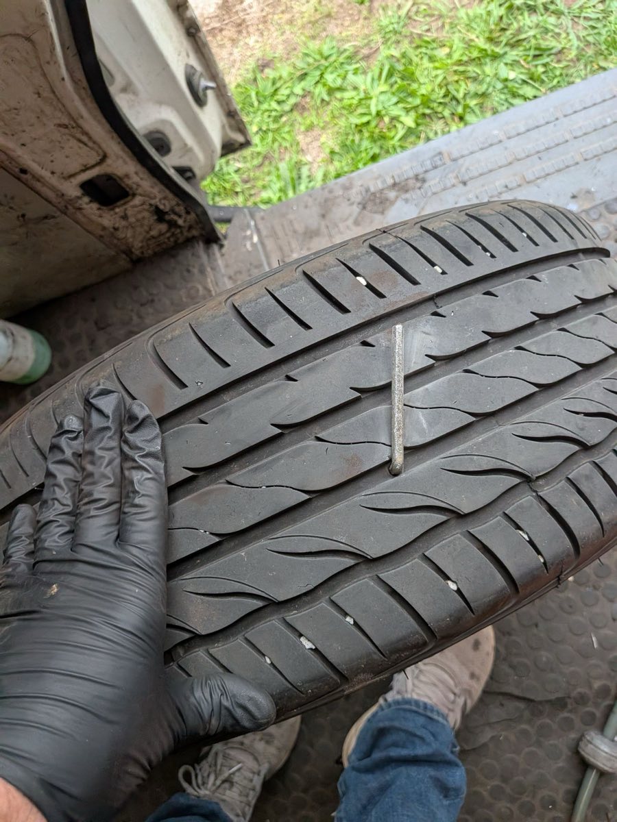 The removed tyre held up by a fitter, with a large Allen key still standing upright through the middle of the tread