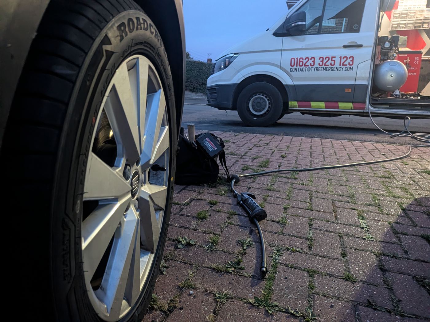 A new tyre fitted on a SEAT alloy wheel on a block-paved drive at dusk, with the Tyre Emergency van and its airline behind